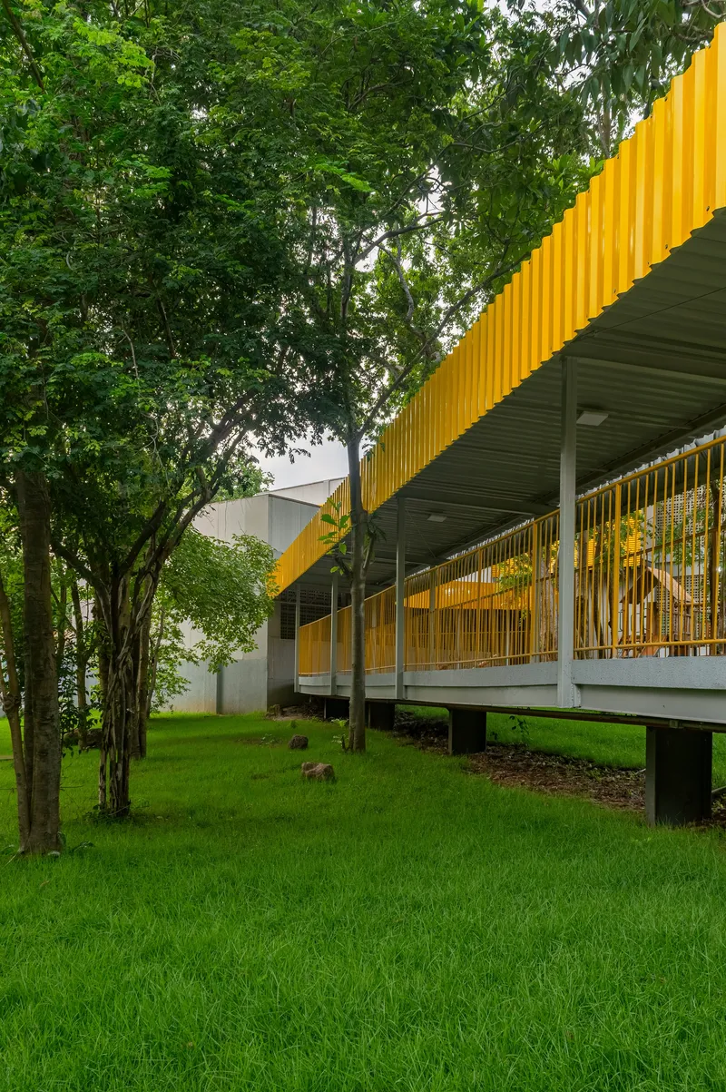 Exterior view of raised walkway with yellow mesh balustrade and ribbed soffit among green trees