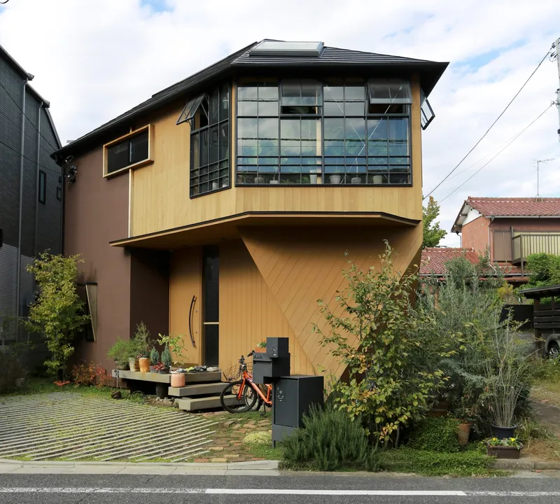 Street view of the cantilevered upper volume clad in pale corrugated metal with gridded windows under cloudy skies