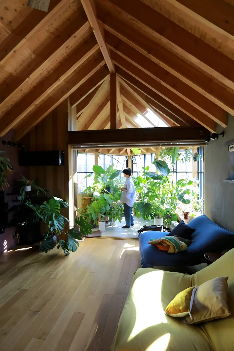 View through the living area toward the glazed sunroom where a person tends to potted plants