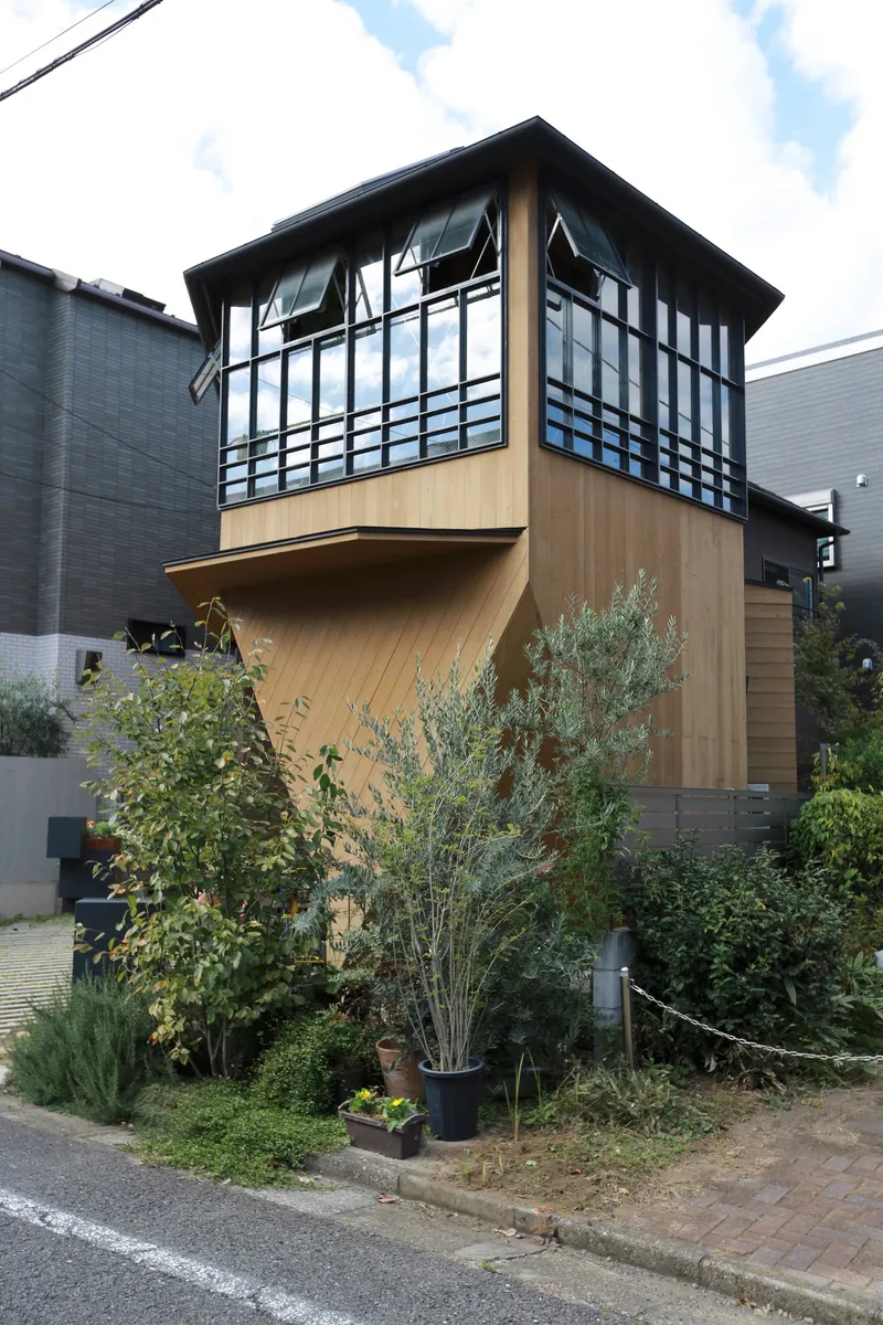 Garden approach showing the projecting upper floor clad in timber above potted plants