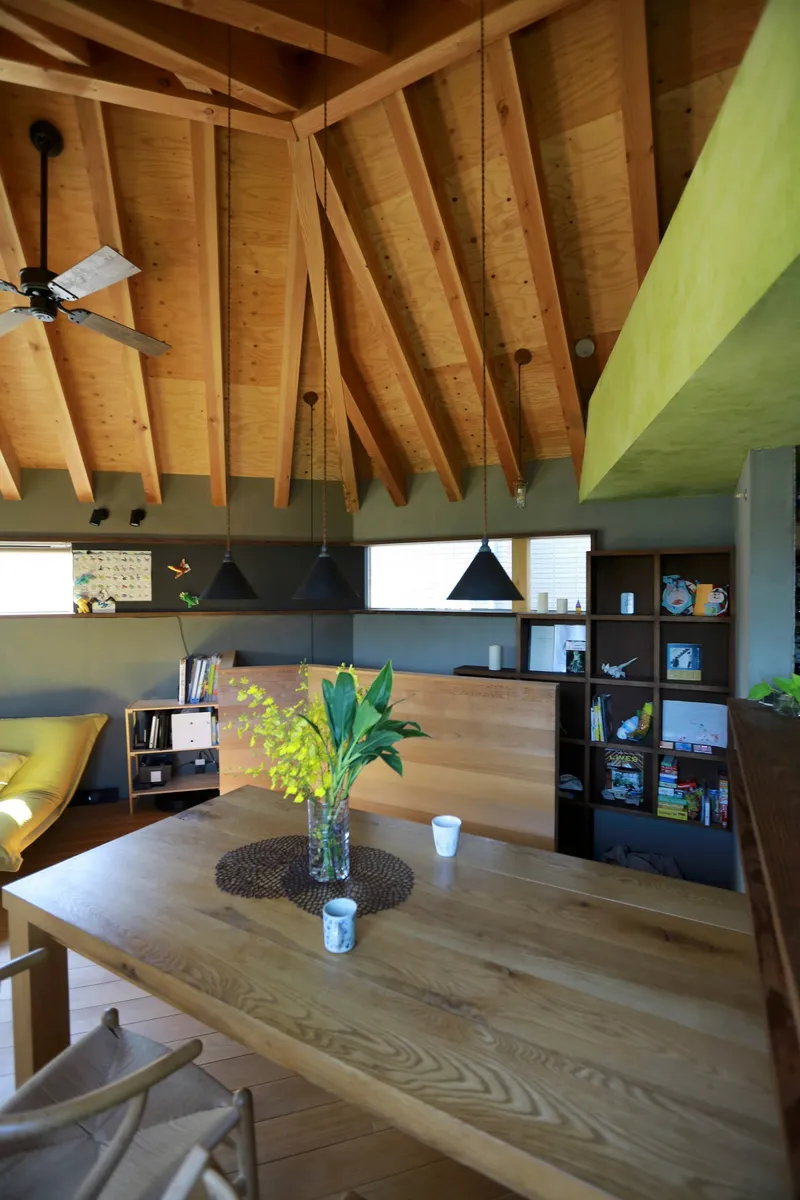 Dining area beneath curving exposed timber beams with black pendant lights and open shelving
