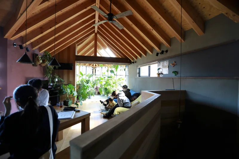 Long view across timber dining table toward inhabitants beneath the vaulted rafter ceiling