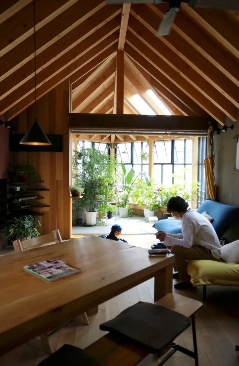 Living room with exposed timber rafters and a person reading on a sofa beside potted plants