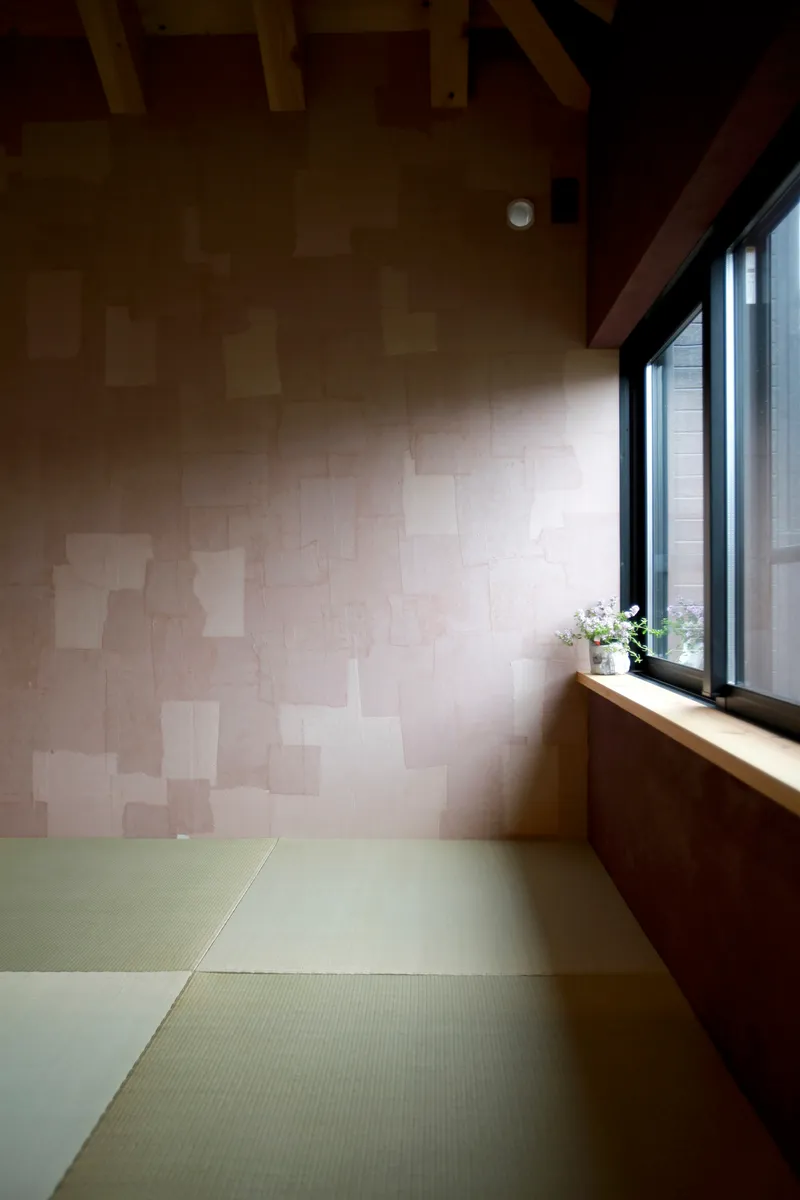Tatami mat floor meeting a patchwork plywood wall beneath a timber beam ceiling