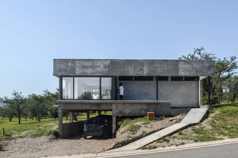 Elevated concrete volume on pilotis with full-height glazing and a figure standing on the terrace