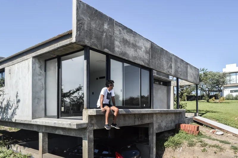 Corner terrace with concrete deck and a person seated at the edge overlooking the carport below