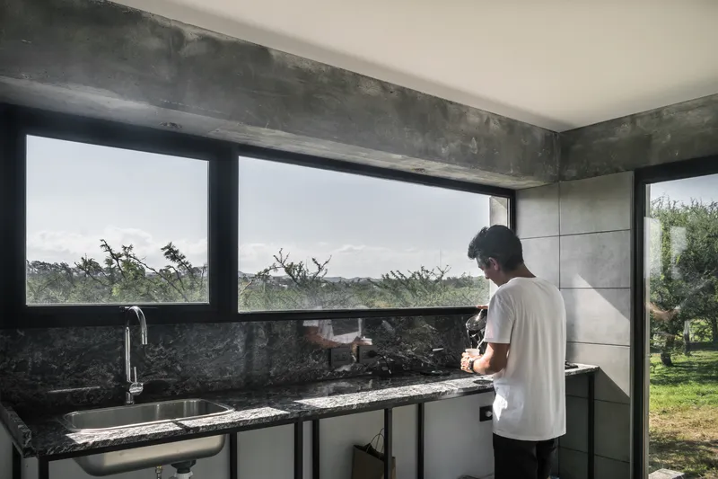 Kitchen with polished stone countertop and horizontal window framing a view of distant trees