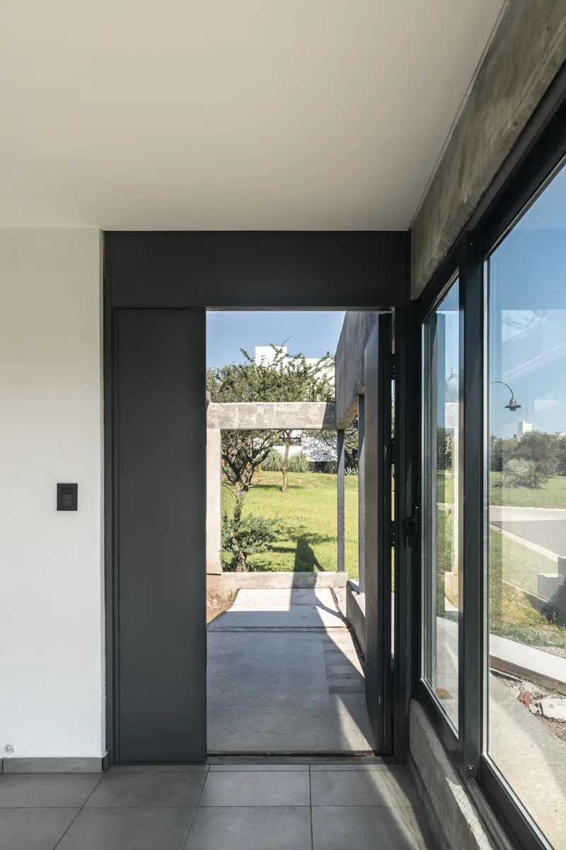 Interior view through black metal framed doorway to concrete courtyard and landscape