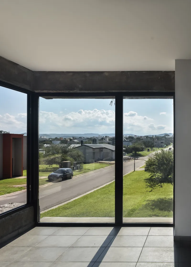 Floor-to-ceiling glazing framing views of suburban street and distant hills under clouded sky