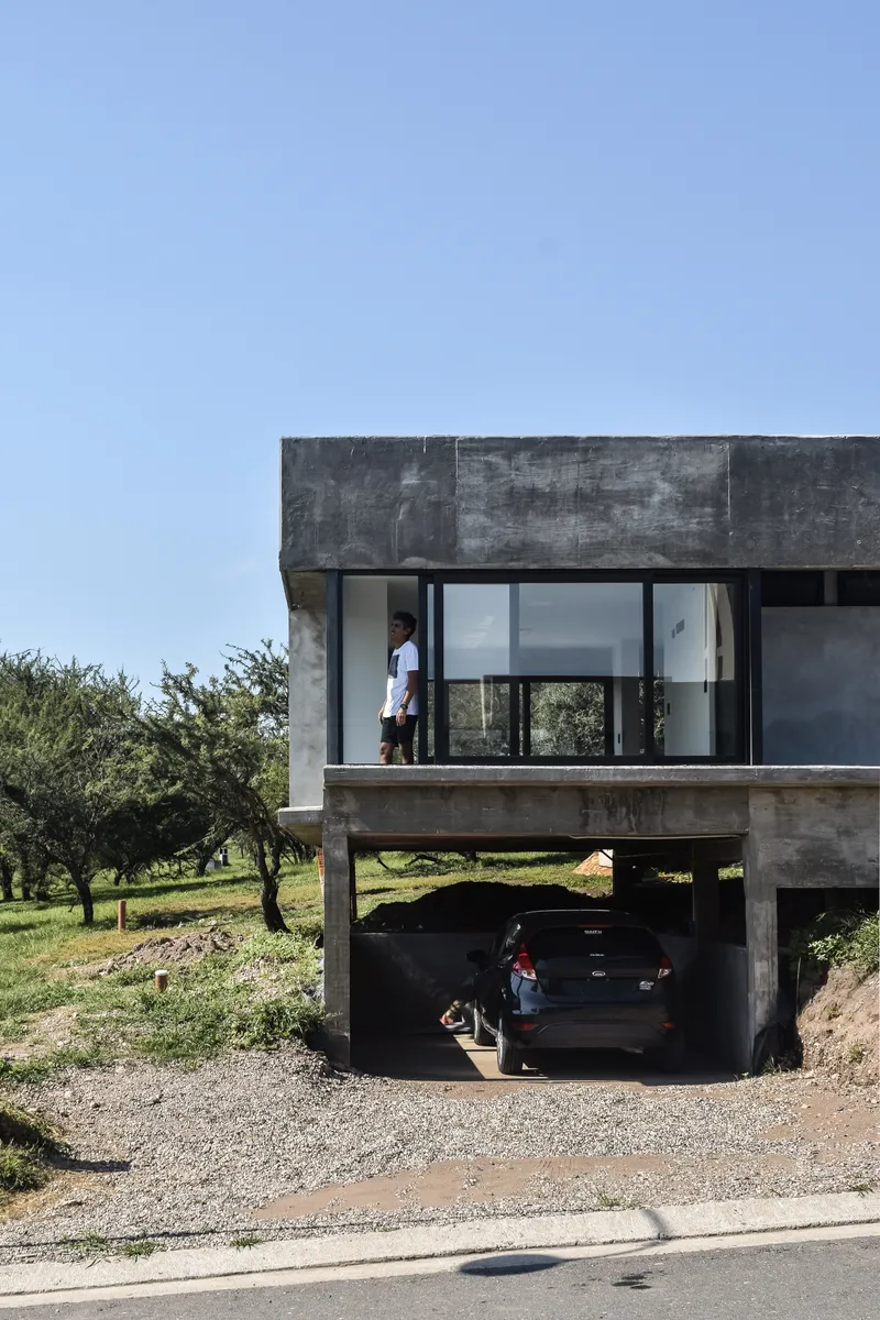Concrete piloti structure supporting the glazed upper level above an open carport with parked car
