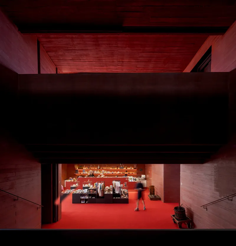 View through a stained timber portal framing the museum shop with a visitor standing on red flooring