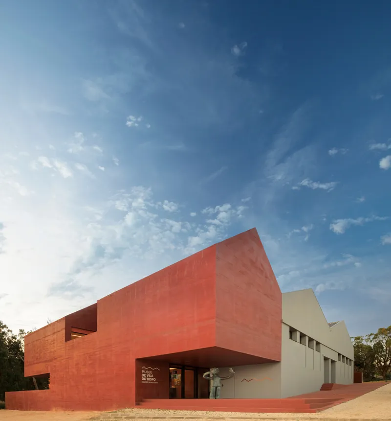 Red clay tile facade with cantilevered volume above the entrance against a clear afternoon sky