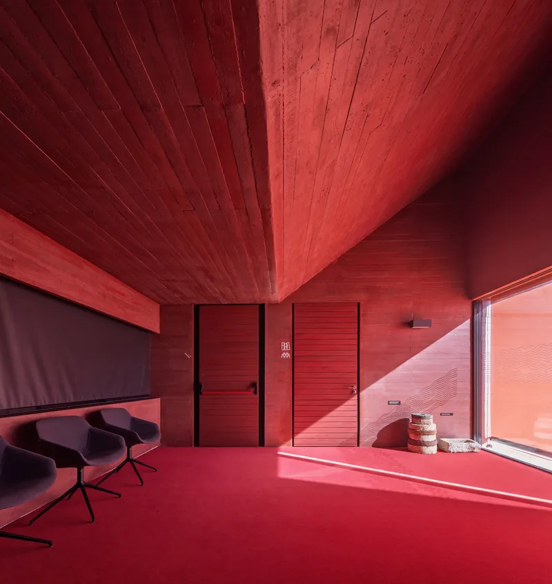 Interior room with red-stained timber walls and ceiling casting warm sunlight across the floor