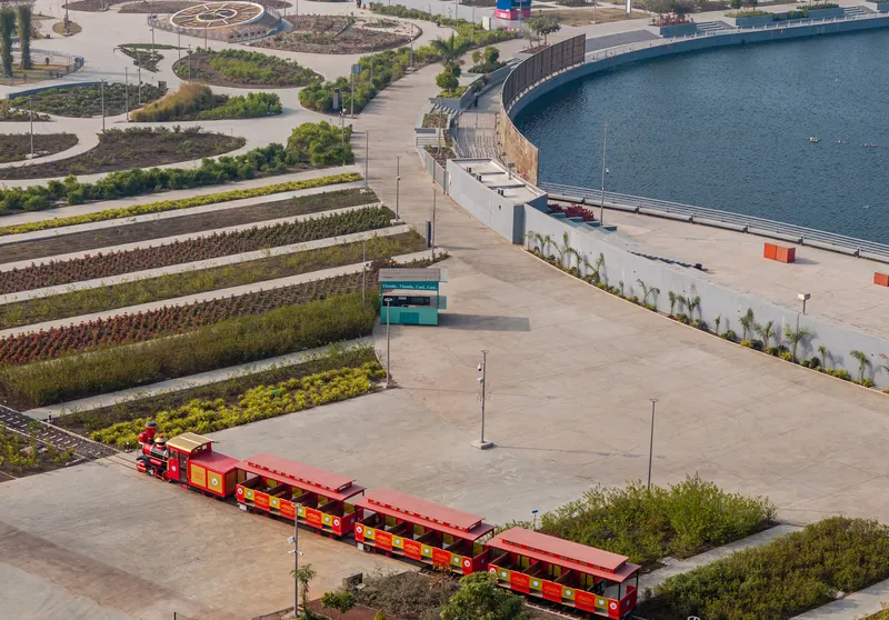 Elevated view of the paved plaza with a red tourist train and planted beds along the water