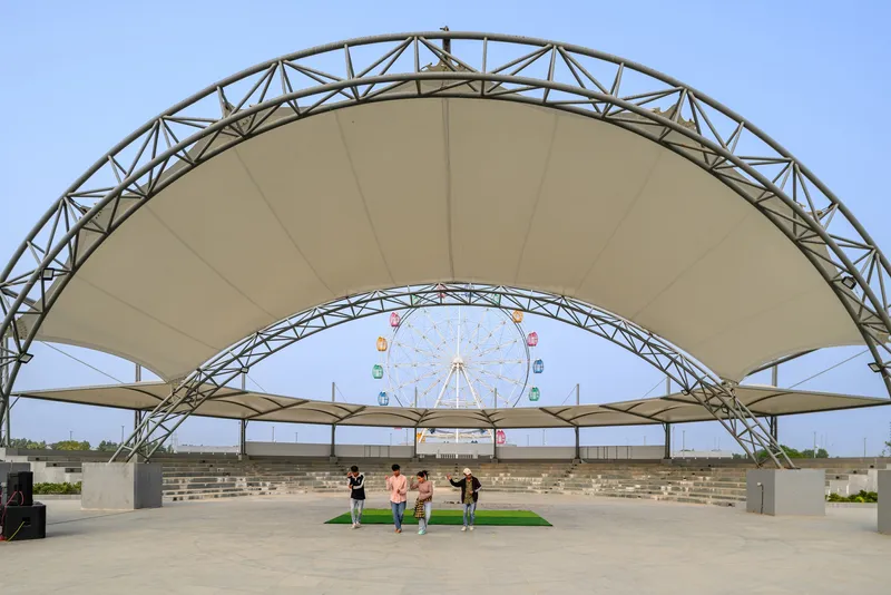 Tensile fabric canopy with exposed steel truss structure framing a distant ferris wheel