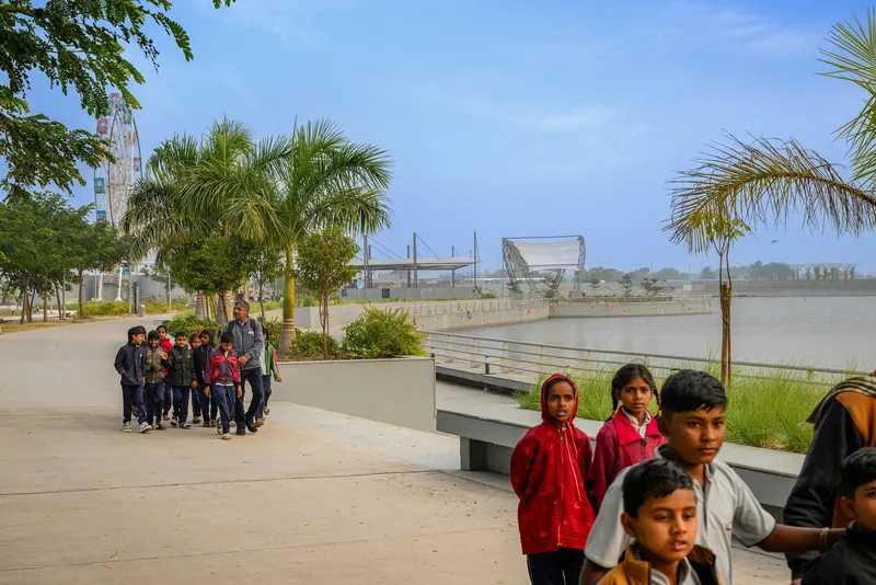 Waterfront promenade with schoolchildren walking past concrete retaining walls and planted beds under palms