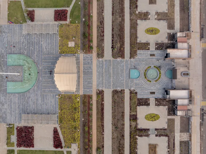 Aerial view of plaza paving pattern with circular fountain, planted beds, and arched canopy structure