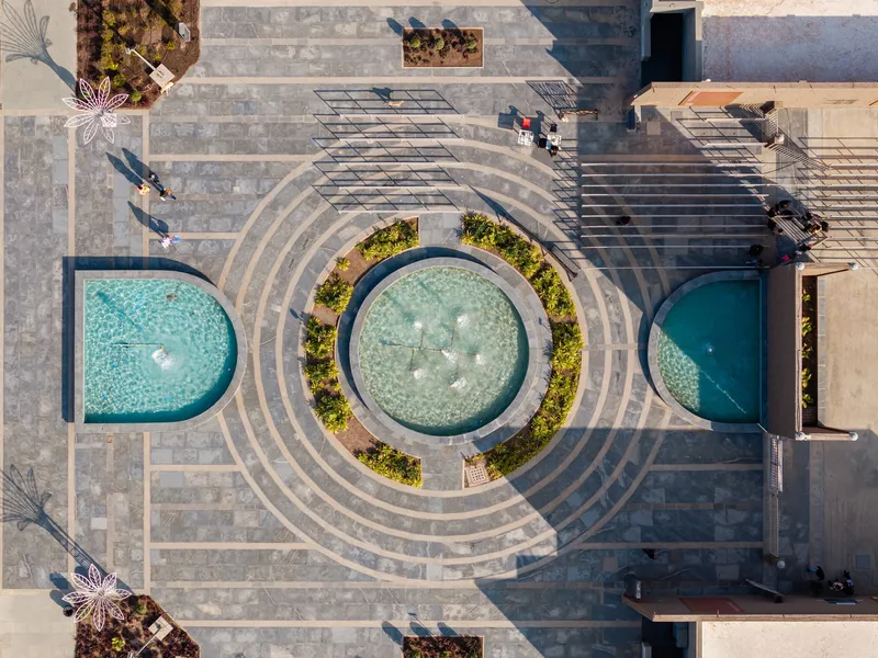 Overhead view of concentric paving rings around central circular fountain flanked by semicircular water features