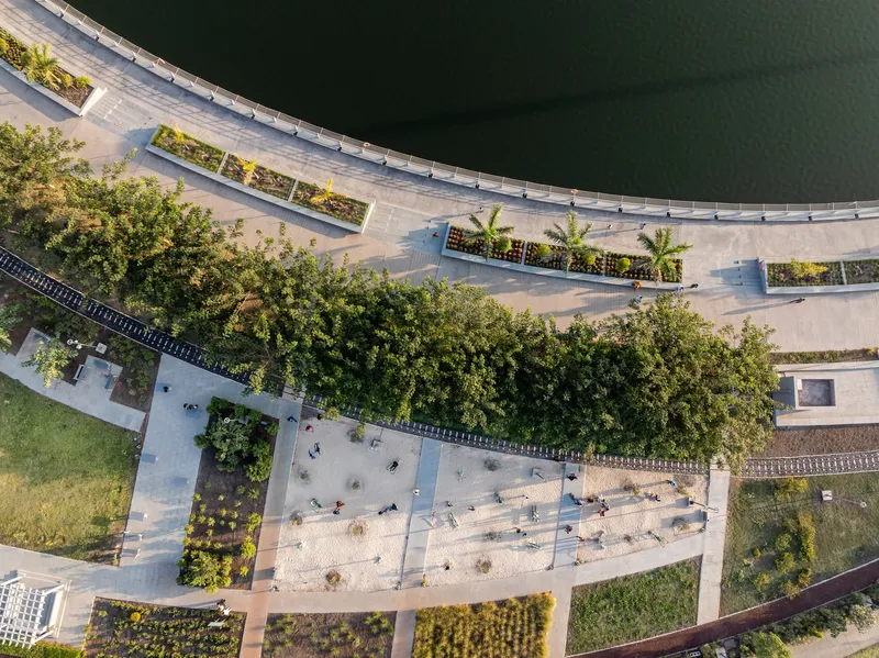 Drone view of the curved waterfront promenade with planted beds and pedestrians along the lake edge