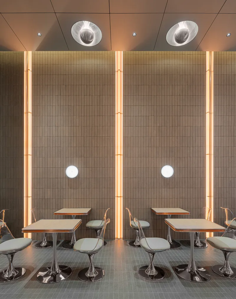 Dining area with fixed tables and chrome swivel chairs beneath vertical LED light strips