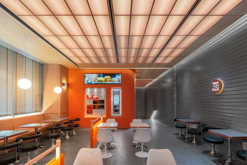 Restaurant interior with backlit gridded ceiling panels and orange service counter with display cases