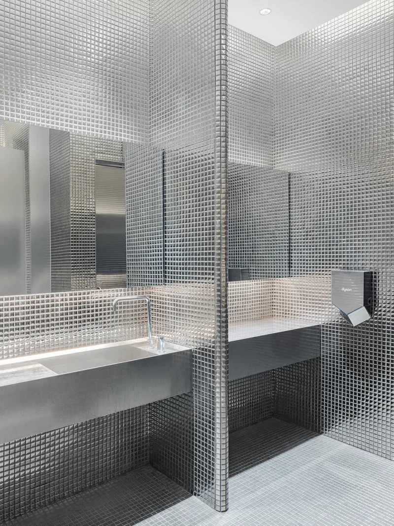 Restroom interior clad in small square mosaic tiles with wall-mounted sink and mirror