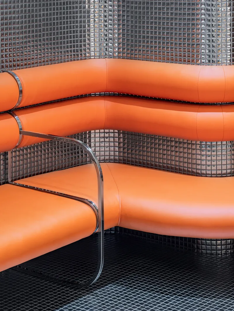 Close-up of orange vinyl booth seating with chrome edge trim against small dark mosaic tile wall