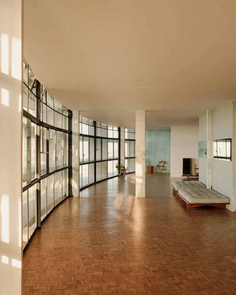 Interior gallery with curved steel-framed glazing casting geometric shadows across the herringbone floor