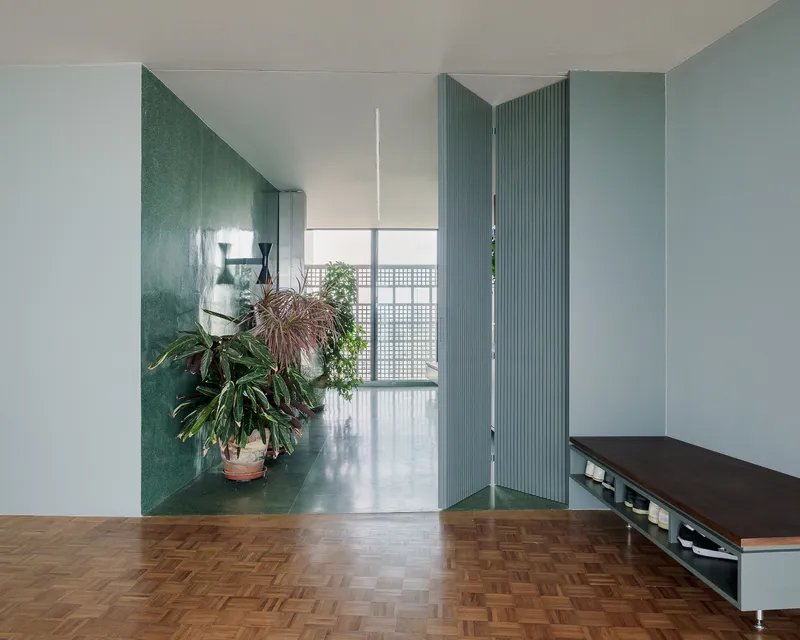 Folding ribbed partition door in blue-green connecting two interior spaces with parquet flooring