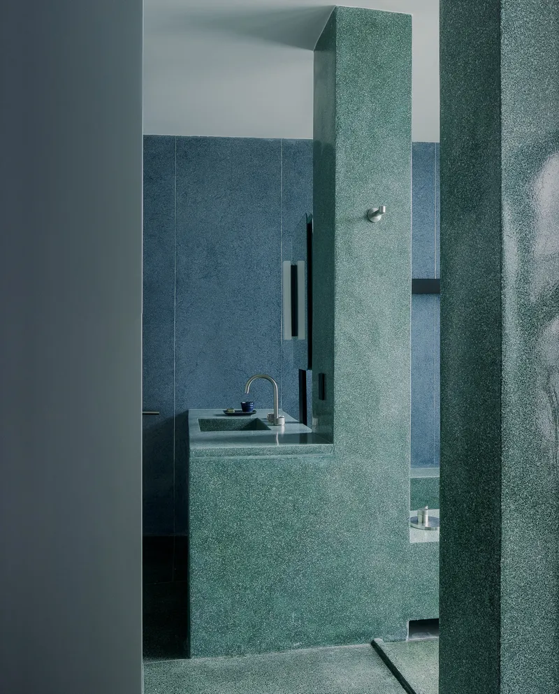 View through teal terrazzo columns into bathroom with floating sink and recessed black storage niches