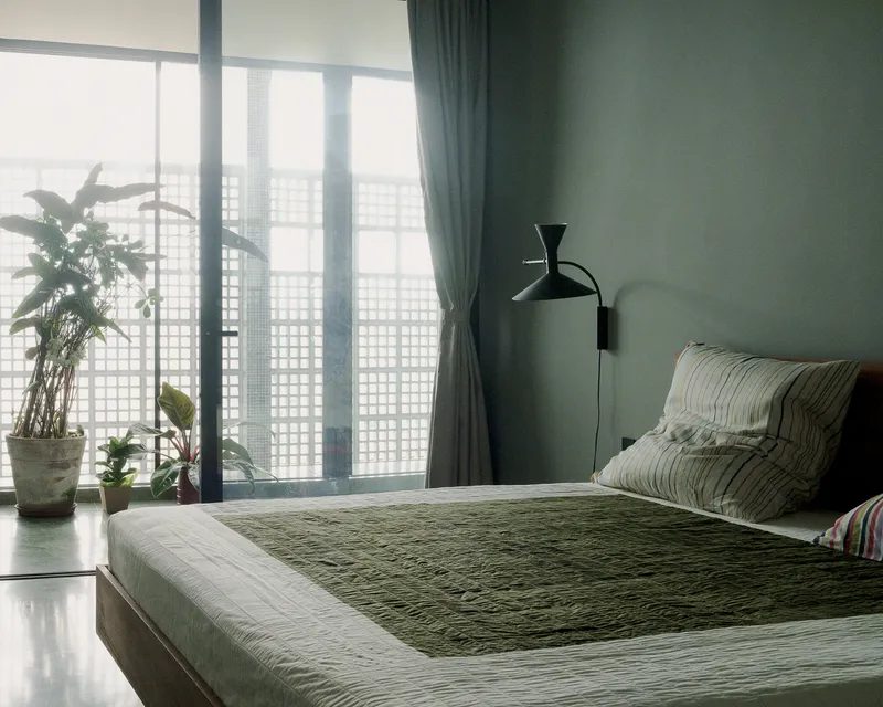 Bedroom with grid-patterned window screen filtering morning light beside potted plants