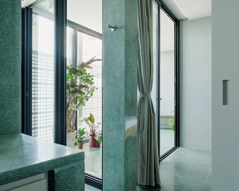 Bathroom corner with green terrazzo wall panels and black-framed windows opening to a planted balcony