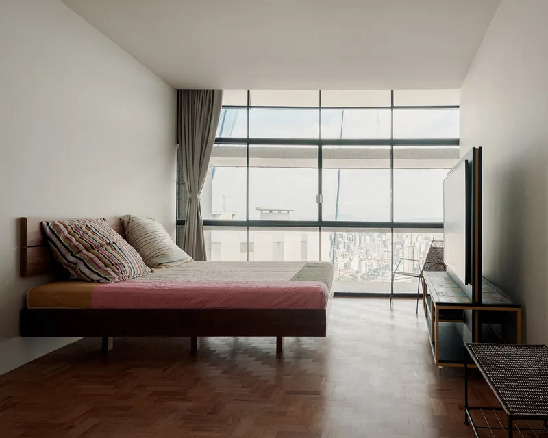Bedroom with herringbone timber floor and full-height glazed wall overlooking the city skyline