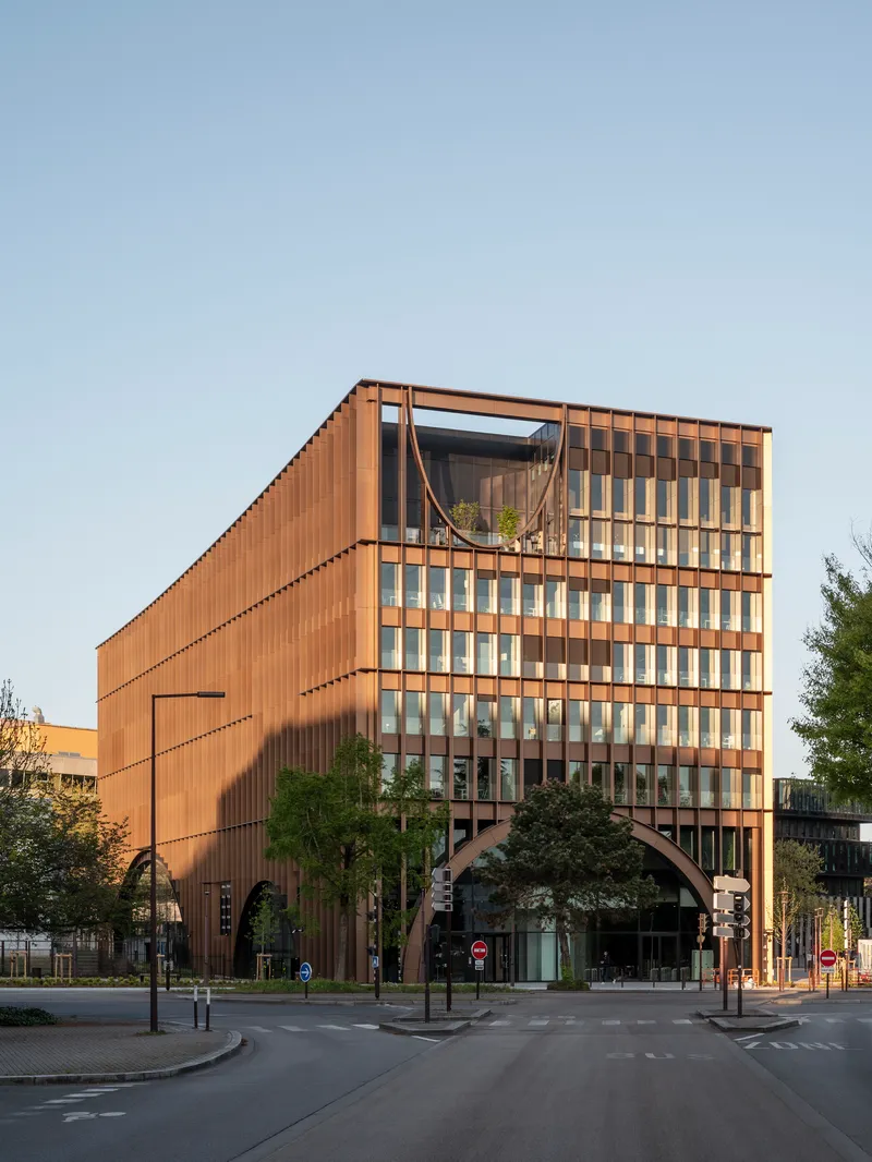 Street view of the copper-toned vertical slat facade with a large arched opening at ground level