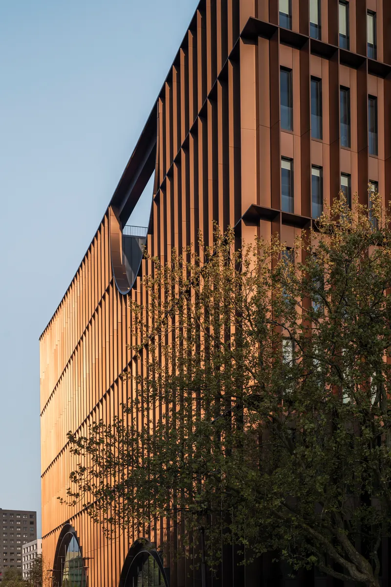 Angled view of the vertical slat facade with a tree partially obscuring the arched entry