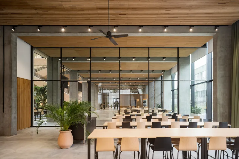 Open canteen interior with timber ceiling panels, concrete columns, potted palms and rows of tables