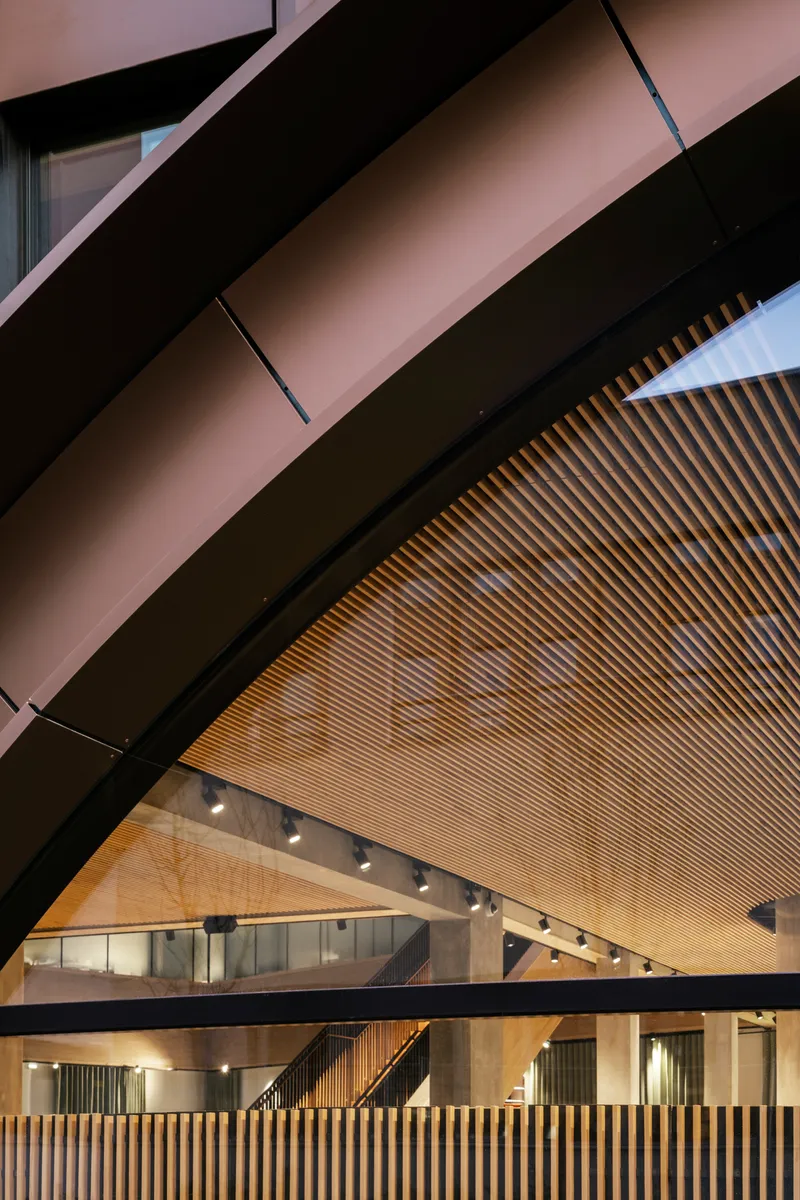 Angular black steel beams intersecting with horizontal timber slat ceiling and concrete balustrade below
