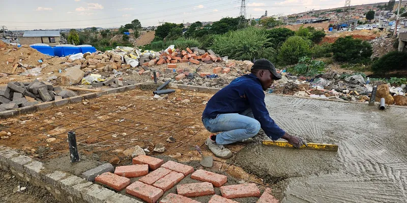 Worker smoothing a fresh concrete slab with red bricks laid out at the edge of the formwork