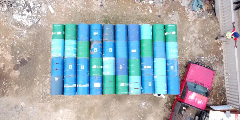 Drone view of blue and green plastic barrels arranged in rows beside a pink vehicle