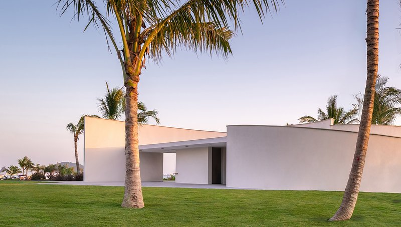 Low horizontal volumes with overhanging roof planes framing openings in a palm grove at dusk