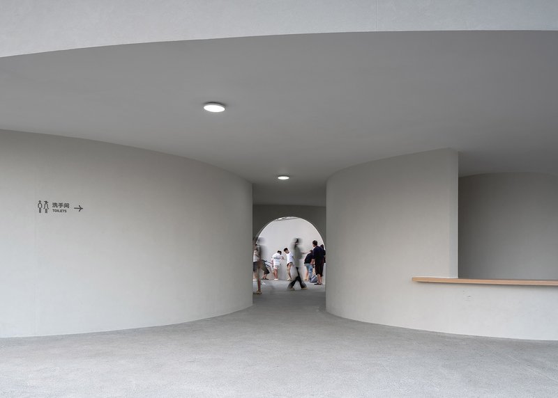 Interior corridor with circular opening and visitors walking through under recessed ceiling lighting