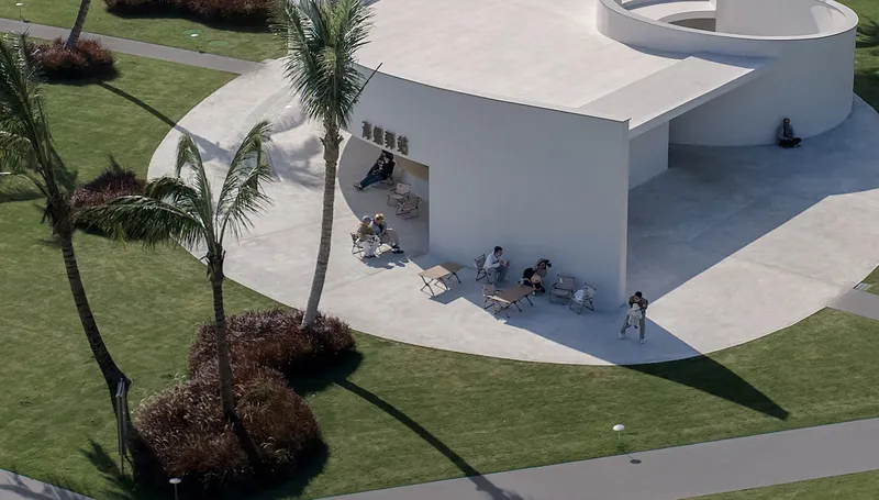 Aerial view of white pavilion with visitors seated on terraces amid palm trees and lawn