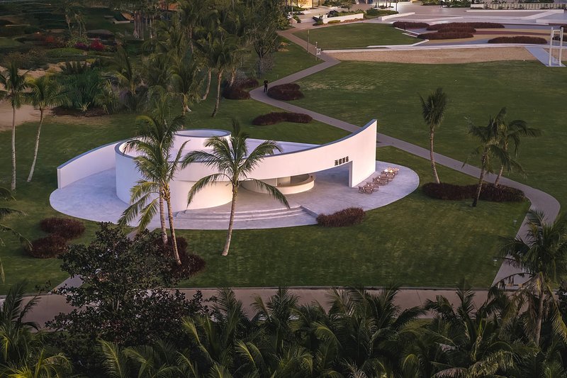 Aerial view of the curving white pavilion surrounded by palm trees and green lawn at dusk