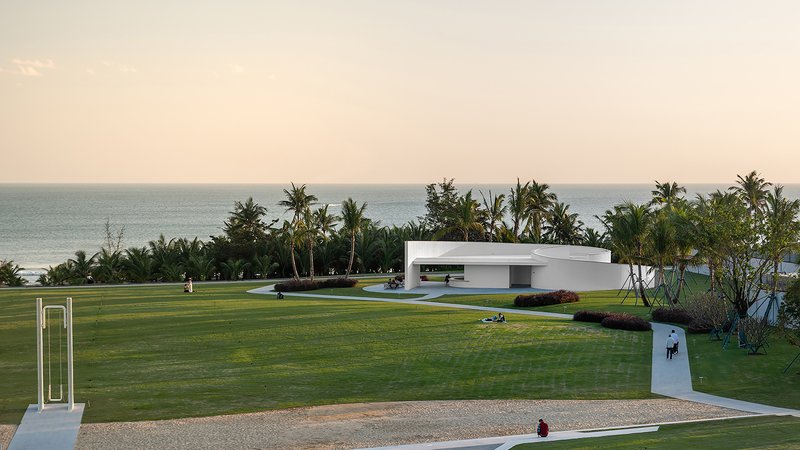 Low horizontal volume with recessed openings set in a mowed lawn facing the ocean at sunset
