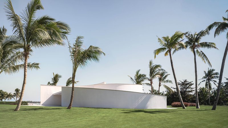 Side elevation of the curved white volume with arched opening beneath swaying palm trees