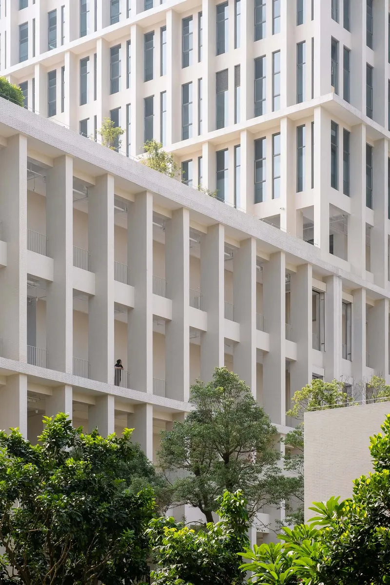 White precast concrete facade with vertical columns and balconies above dense landscaping at the podium