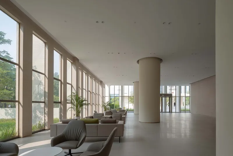 Lobby interior with tall floor-to-ceiling windows, cylindrical column and scattered lounge seating under soft daylight