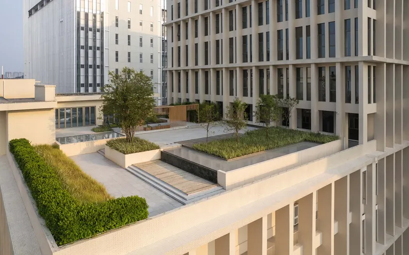 Elevated terrace with raised planted beds, trees and hedges between white precast facades