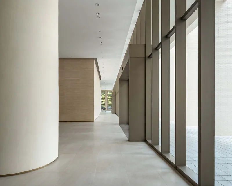 Lobby corridor with curved white column, bronze metal screens and pale stone flooring
