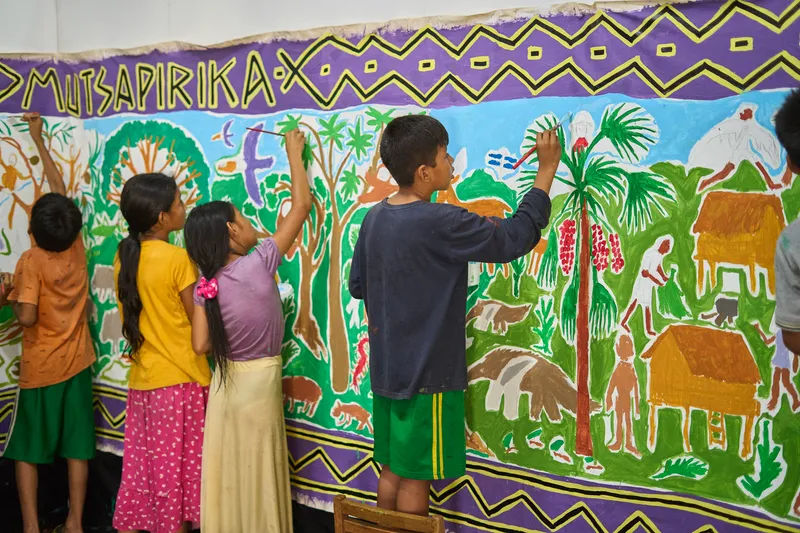 Children painting a mural depicting tropical vegetation and animals on an interior wall panel